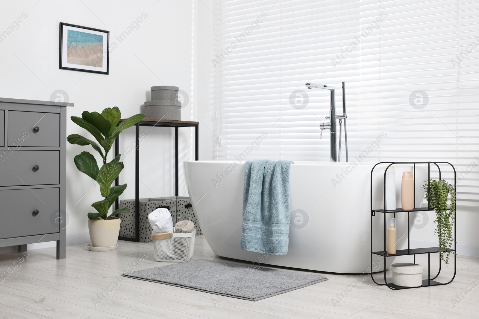 Photo of Stylish bathroom interior with bath tub, houseplants and soft light grey mat