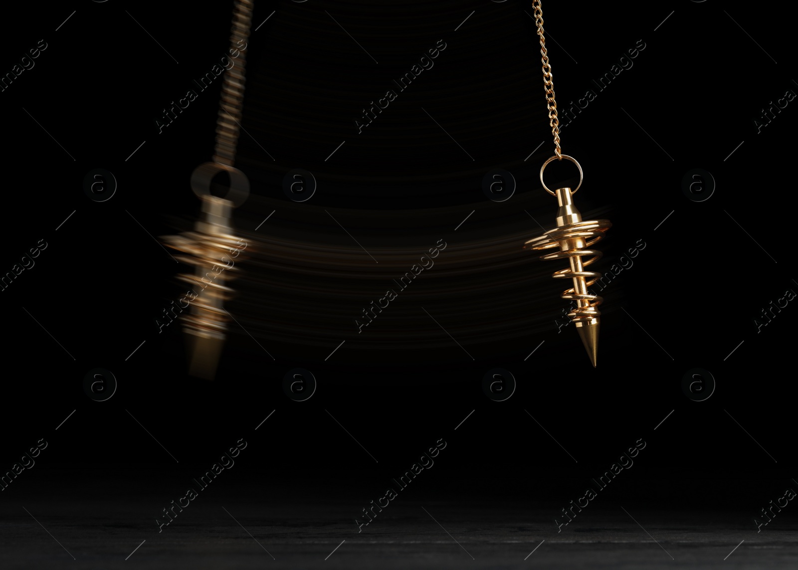 Image of Hypnosis session. Pendant swinging over surface on black background, motion effect