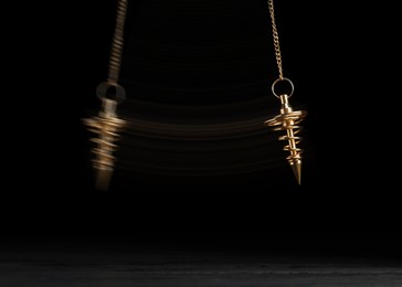 Image of Hypnosis session. Pendant swinging over surface on black background, motion effect
