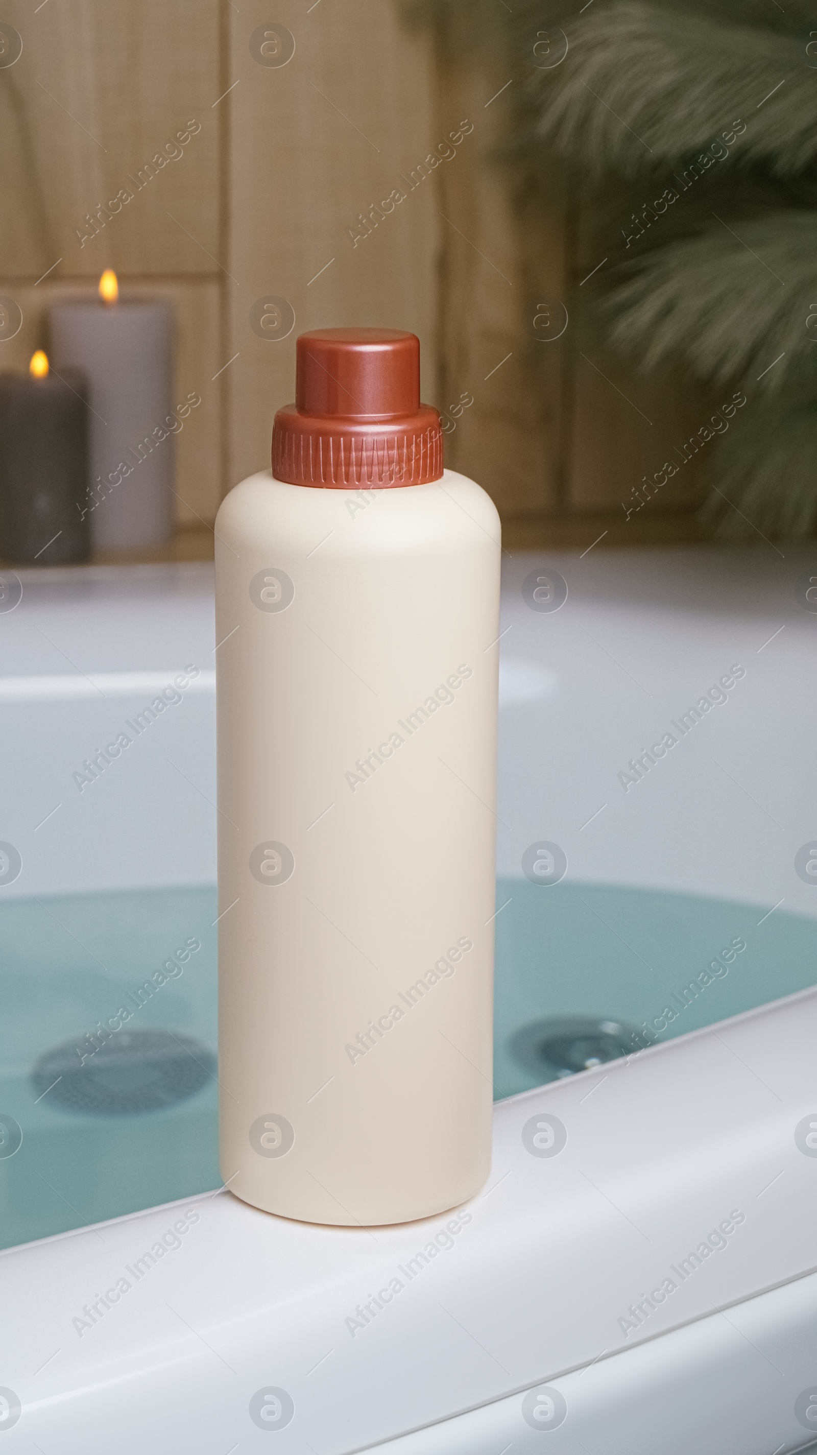 Photo of Beige bottle of bubble bath and candles on tub indoors