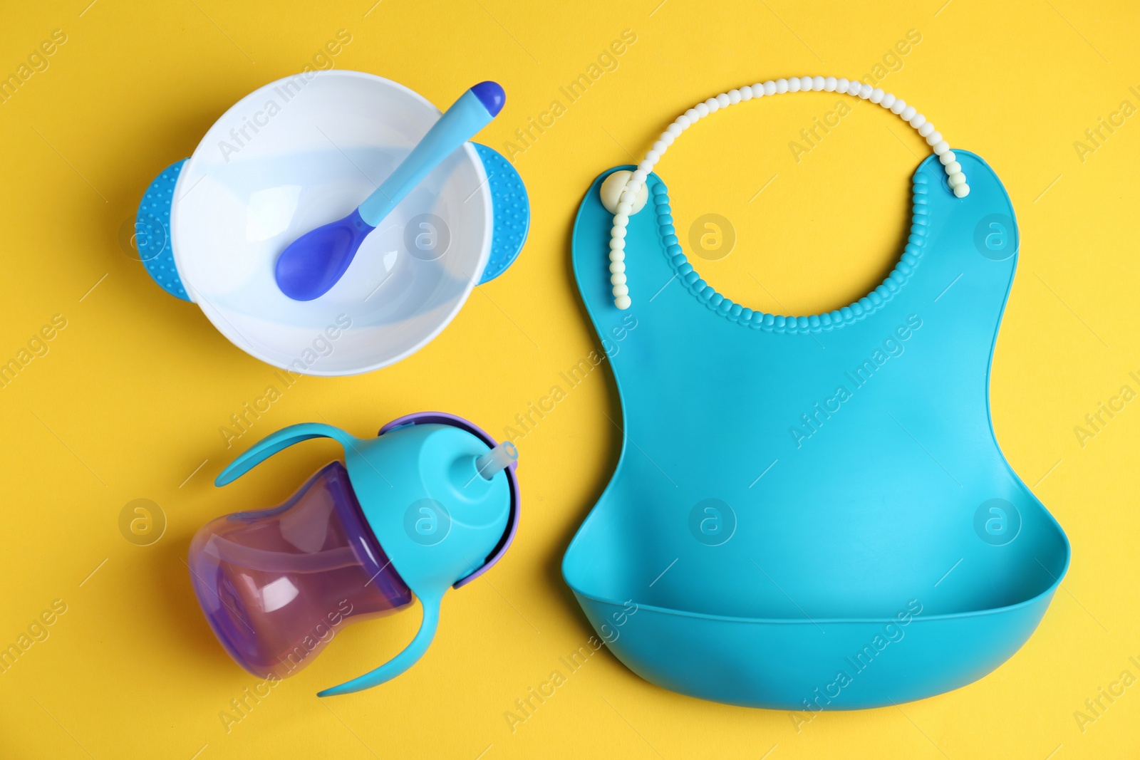 Photo of Set of colorful plastic dishware and silicone bib on yellow background, flat lay. Serving baby food