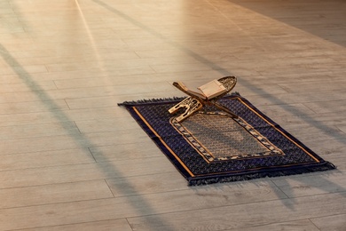 Photo of Rehal with open Quran on Muslim prayer mat indoors. Space for text