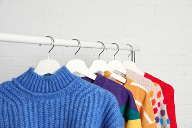 Collection of warm sweaters hanging on rack against white brick wall