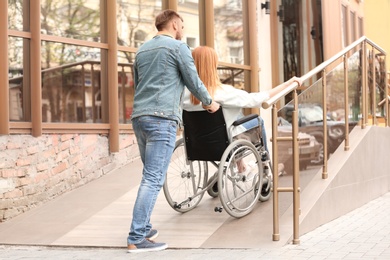 Photo of Woman in wheelchair and man using ramp outdoors