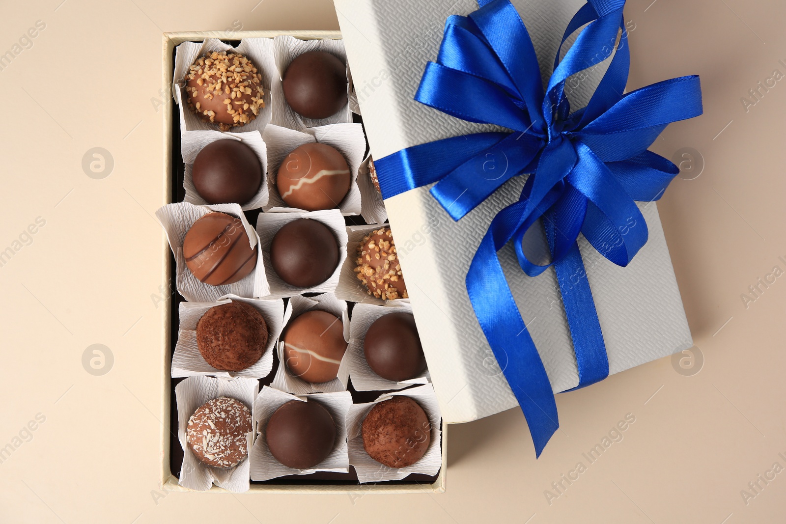 Photo of Box with delicious chocolate candies on beige background, top view