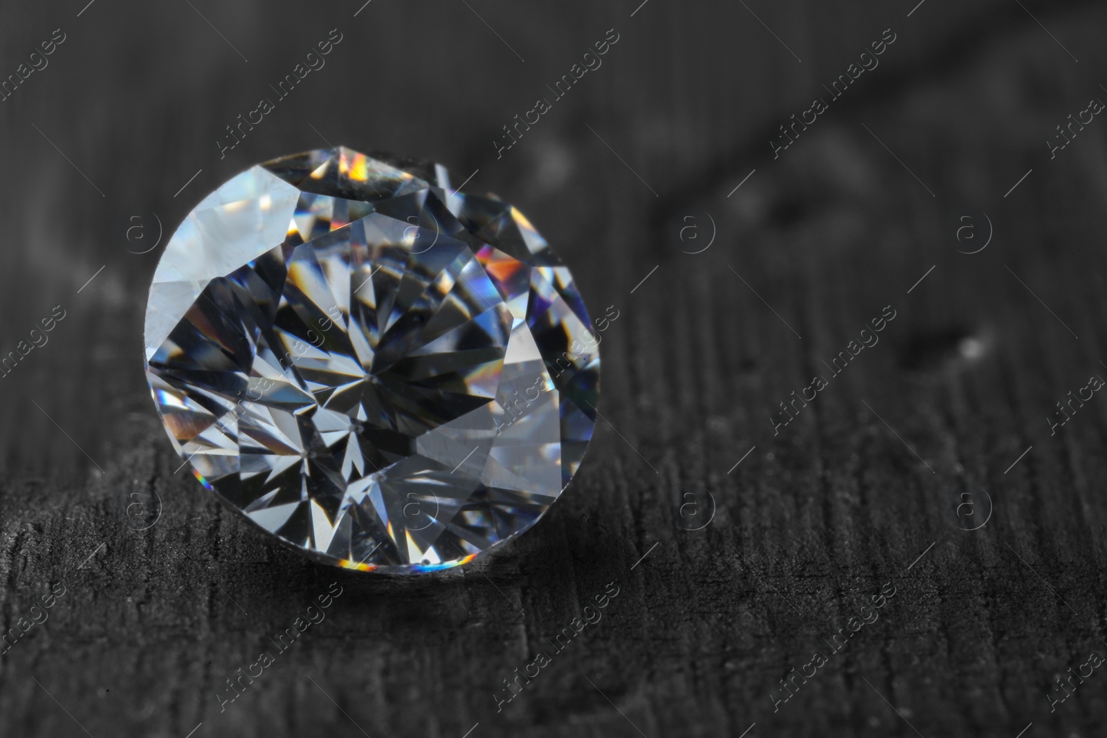 Photo of Beautiful shiny diamond on dark gray table, closeup. Space for text