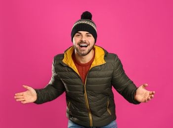 Happy young man in warm clothes on pink background. Winter vacation