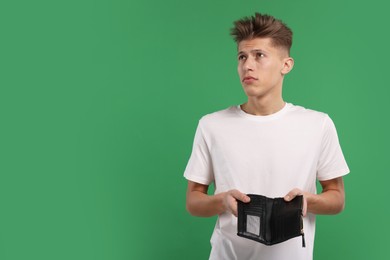 Photo of Upset man with empty wallet on green background. Space for text