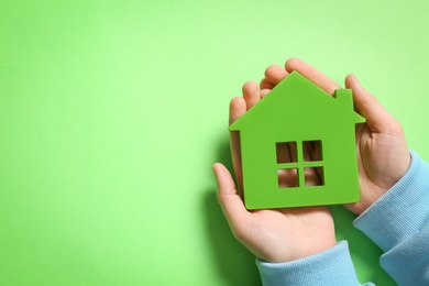 Photo of Woman holding house model on light green background, top view. Space for text