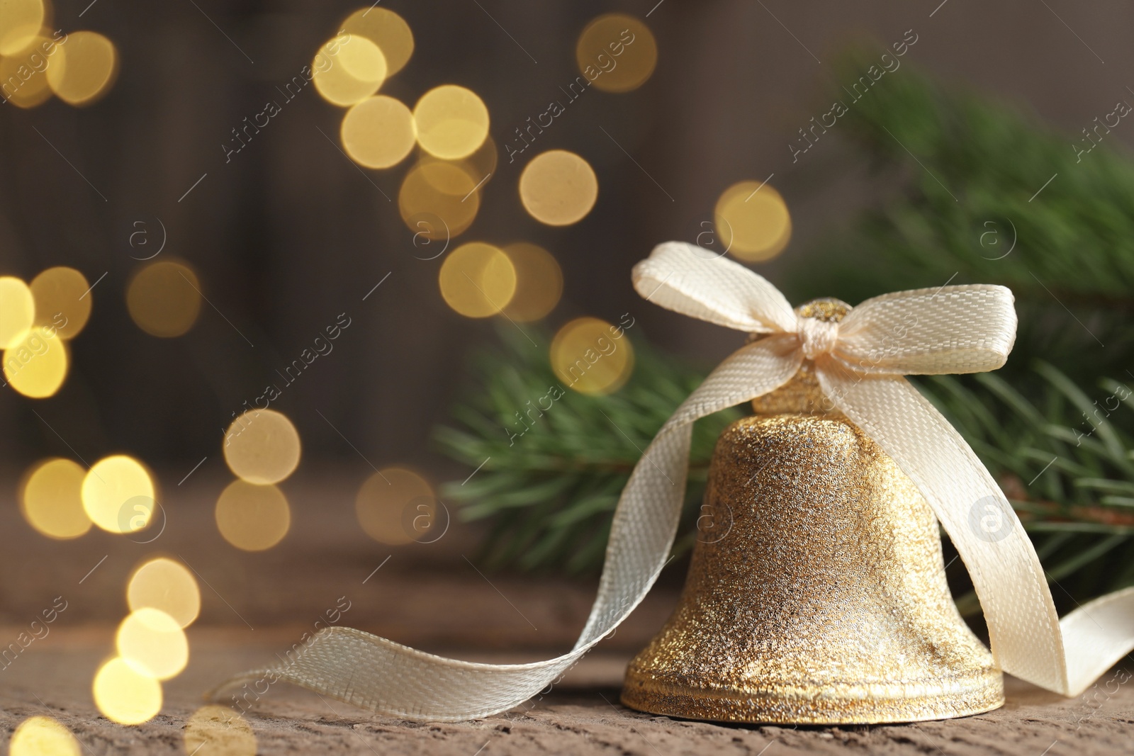 Photo of Bell and fir tree branches on wooden table, closeup with space for text. Christmas decor