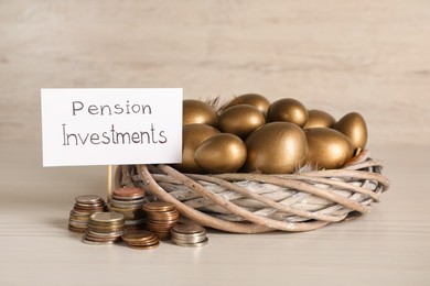 Photo of Golden eggs in nest, coins and card with phrase Pension Investments on white wooden table