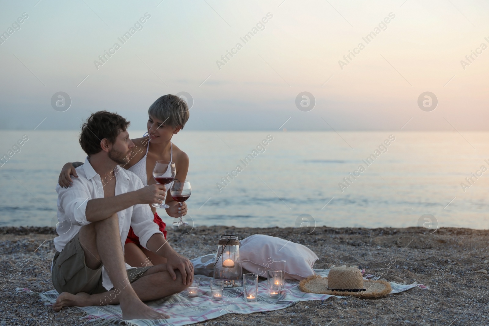 Photo of Young couple with wine and candles on beach. Space for text