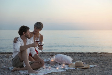 Young couple with wine and candles on beach. Space for text