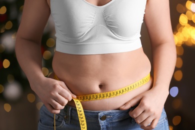 Photo of Woman with measuring tape indoors, closeup. Overweight problem after New Year party