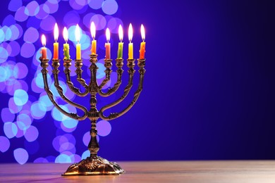Hanukkah celebration. Menorah with burning candles on table against blue background with blurred lights, space for text
