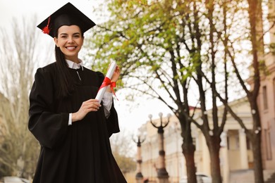 Photo of Happy student with diploma after graduation ceremony outdoors. Space for text