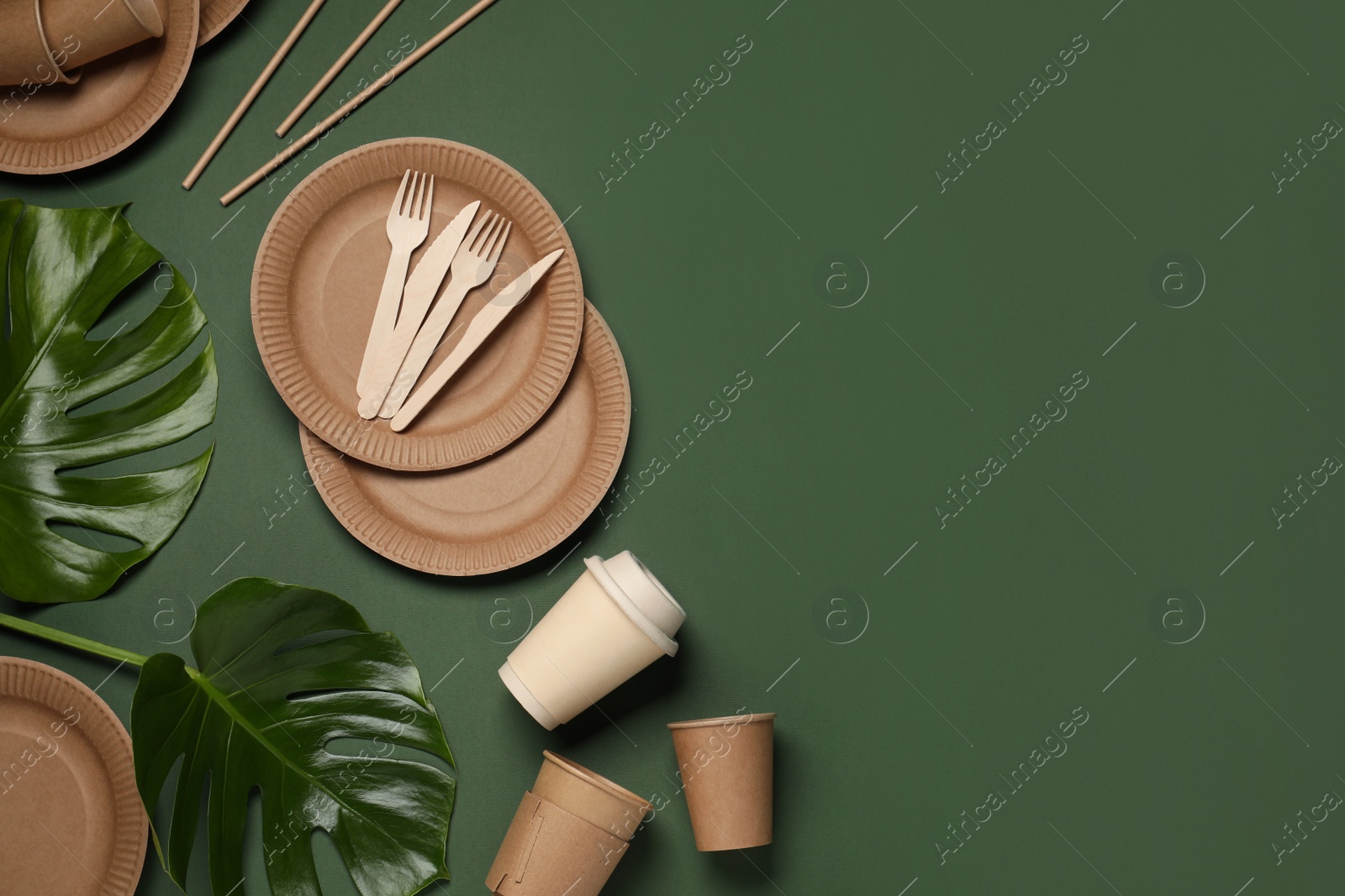 Photo of Flat lay composition with disposable tableware and monstera leaves on dark green background. Space for text