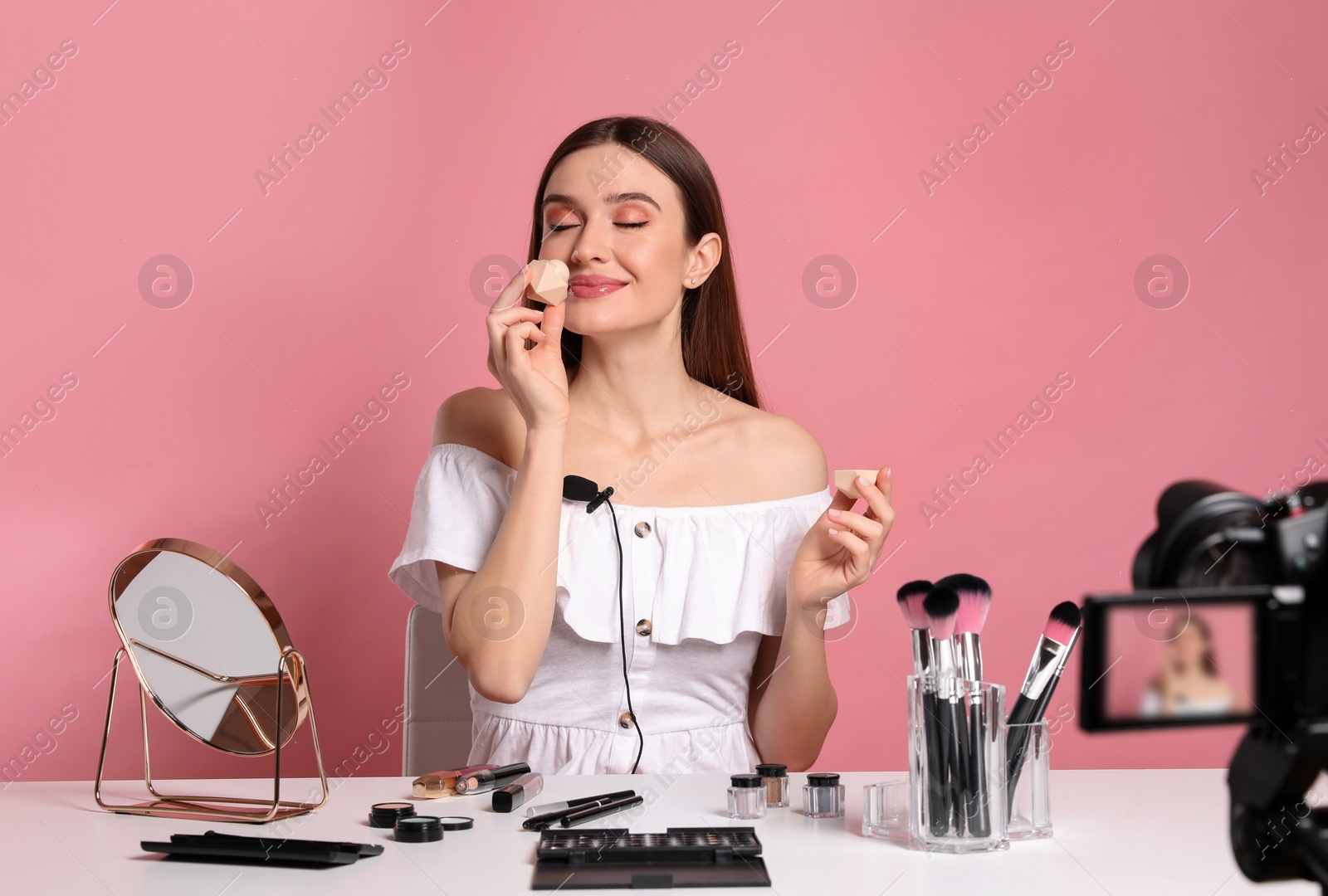 Photo of Beauty blogger recording makeup tutorial on pink background