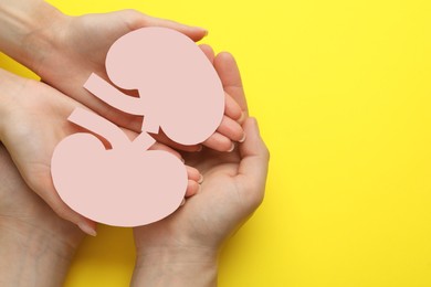 People holding paper cutout of kidneys on yellow background, top view. Space for text