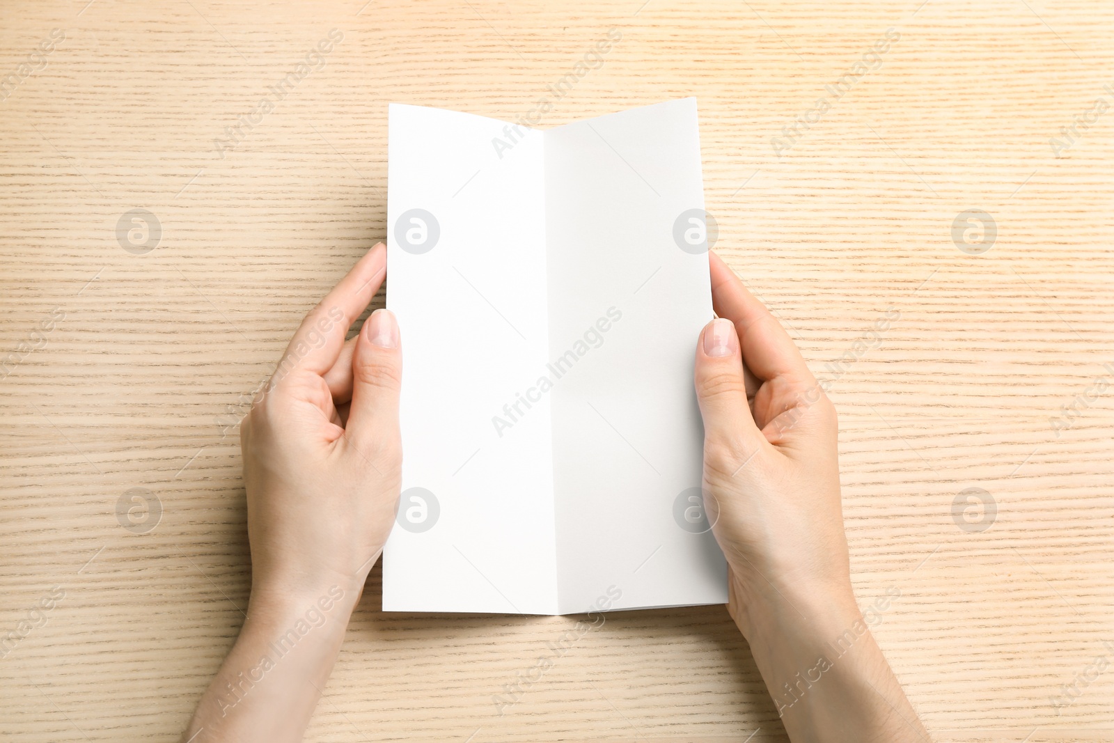 Photo of Young woman holding blank brochure at light wooden table, top view. Mock up for design