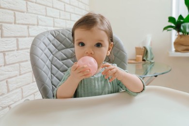 Cute little baby nibbling toy in high chair indoors