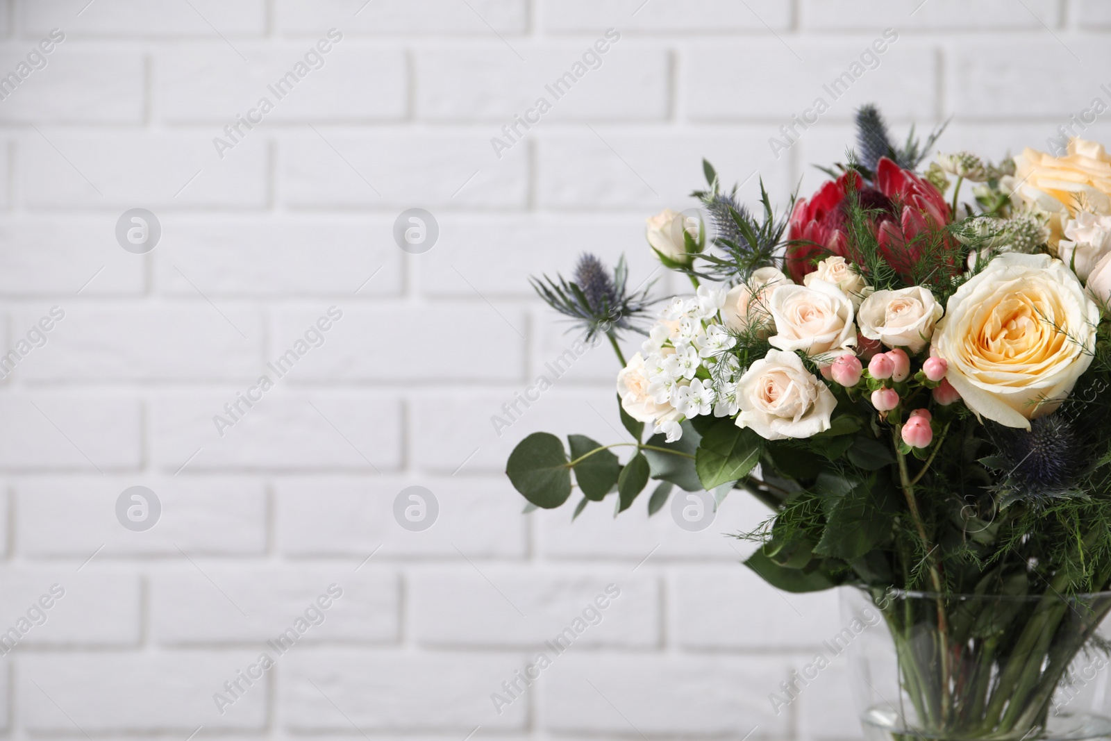 Photo of Beautiful bouquet with roses against white brick wall, closeup. Space for text