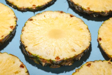 Photo of Slices of tasty ripe pineapple on light blue background, closeup