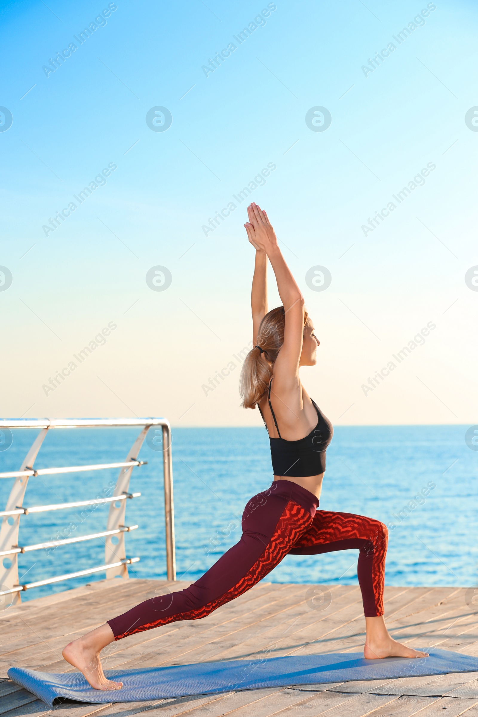 Photo of Young woman doing yoga exercises on pier in morning