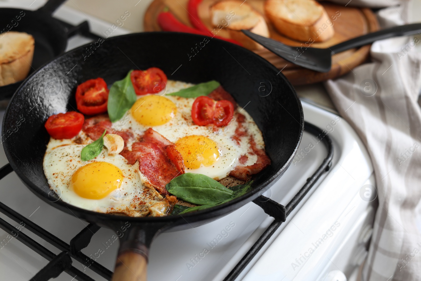 Photo of Delicious fried eggs with bacon and tomatoes in pan on stove