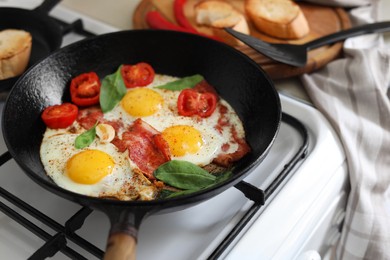 Photo of Delicious fried eggs with bacon and tomatoes in pan on stove