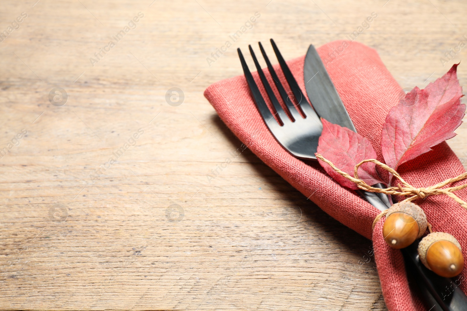 Photo of Cutlery with acorns, autumn leaves and napkin on wooden table, space for text. Thanksgiving Day