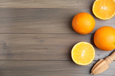 Photo of Fresh ripe oranges and reamer on wooden table, flat lay. Space for text