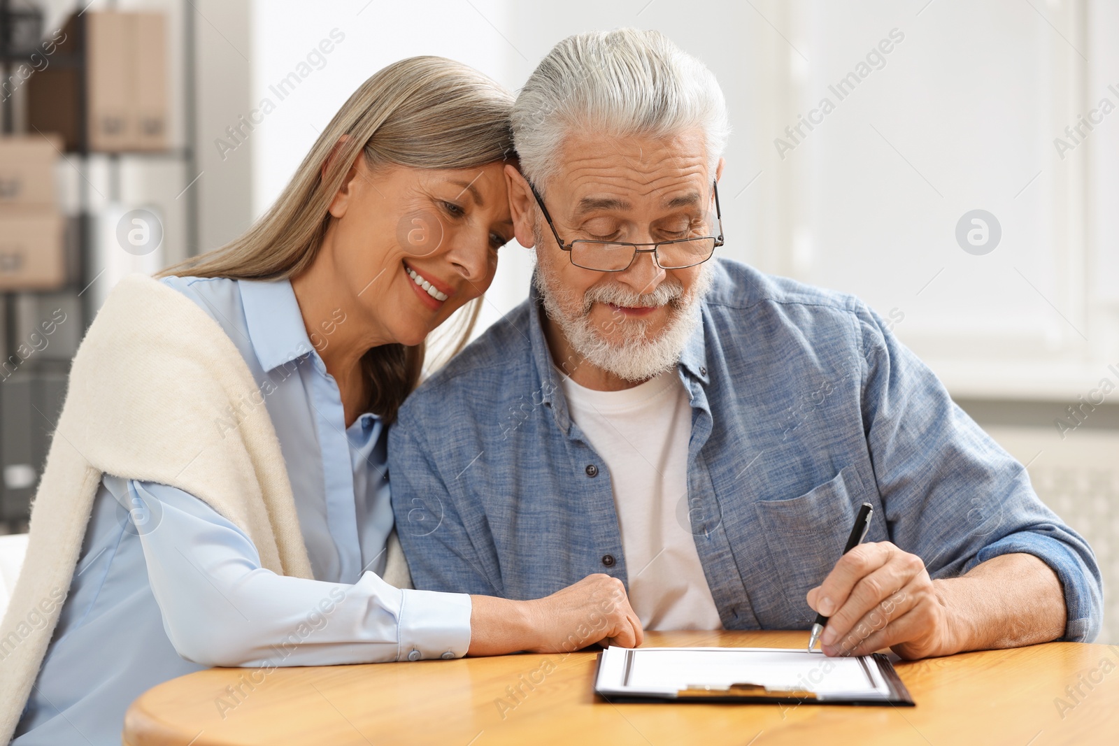 Photo of Happy senior couple signing Last Will and Testament indoors