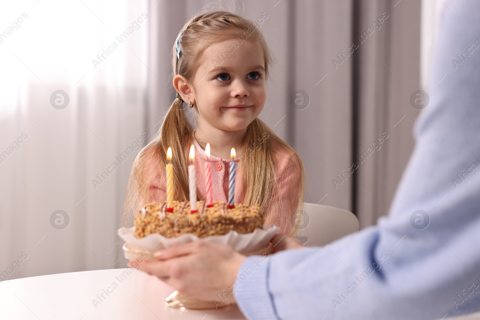 Photo of Birthday celebration. Mother holding tasty cake with burning candles near her daughter indoors