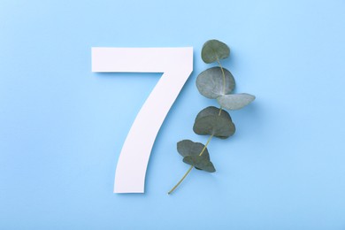 Photo of Paper number 7 and eucalyptus branch on light blue background, top view