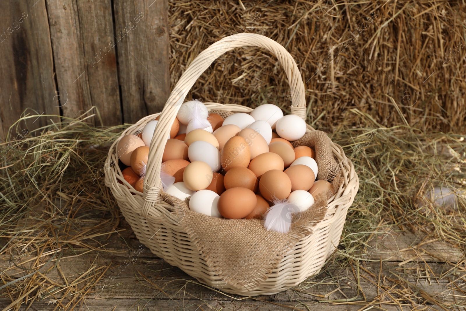 Photo of Wicker basket with fresh chicken eggs and dried straw in henhouse