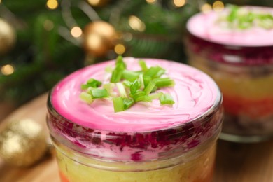 Glass jars with herring under fur coat and Christmas decor on wooden table, closeup. Traditional Russian salad