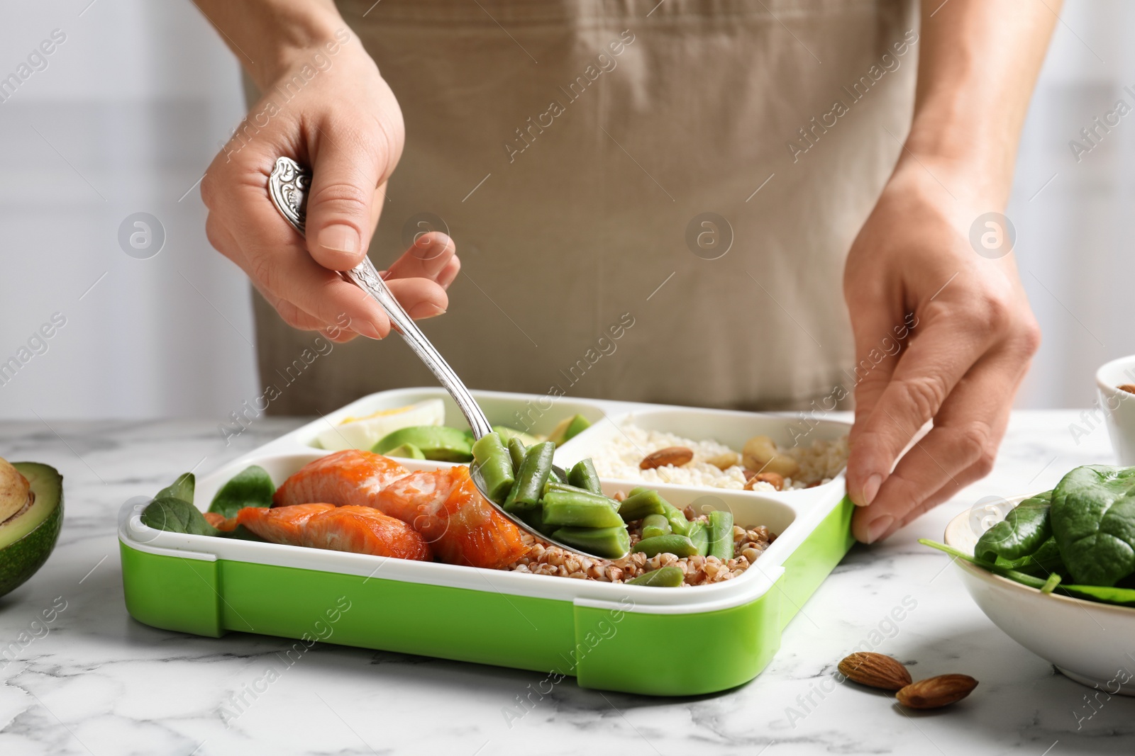 Photo of Woman putting natural protein food into container on marble table, closeup