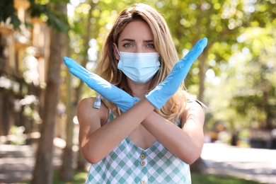 Photo of Woman in protective face mask showing stop gesture outdoors. Prevent spreading of coronavirus