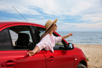 Photo of Happy woman leaning out of car window on beach. Summer vacation trip