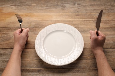 Photo of Man with cutlery and empty plate at wooden table, closeup