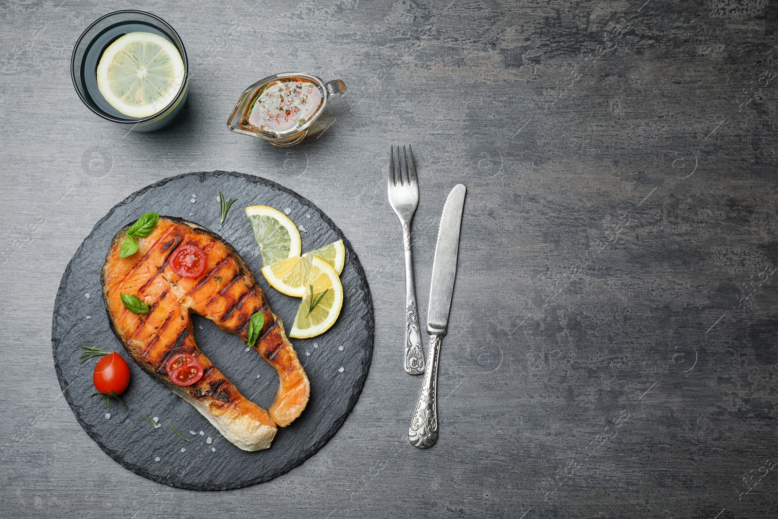 Photo of Slate plate with tasty salmon steak on grey background