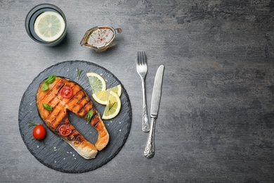 Photo of Slate plate with tasty salmon steak on grey background