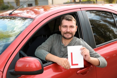 Man showing learner driver sign from new car. Get driving license