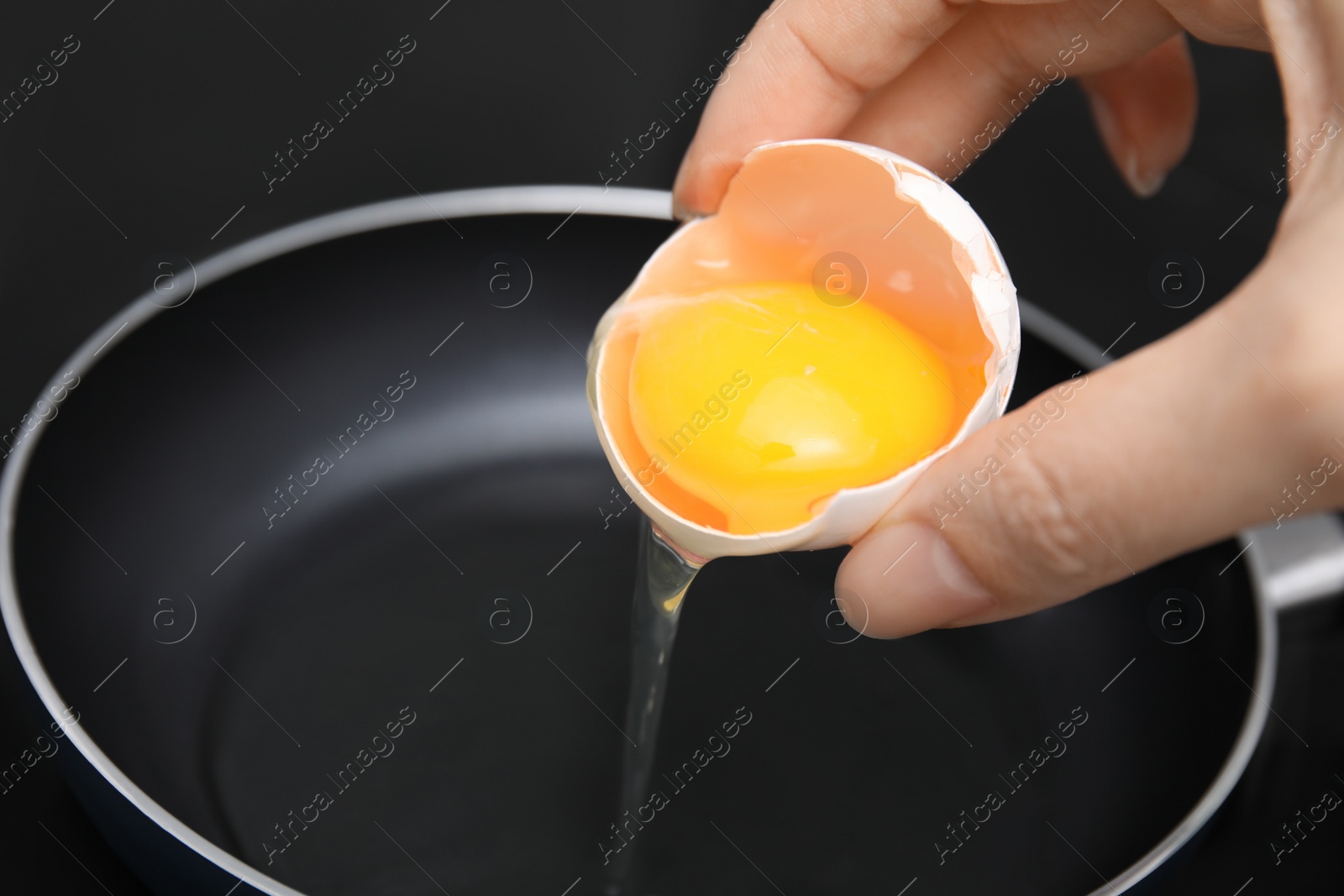 Photo of Woman adding raw egg into frying pan, closeup