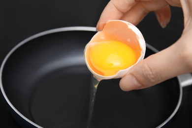 Photo of Woman adding raw egg into frying pan, closeup