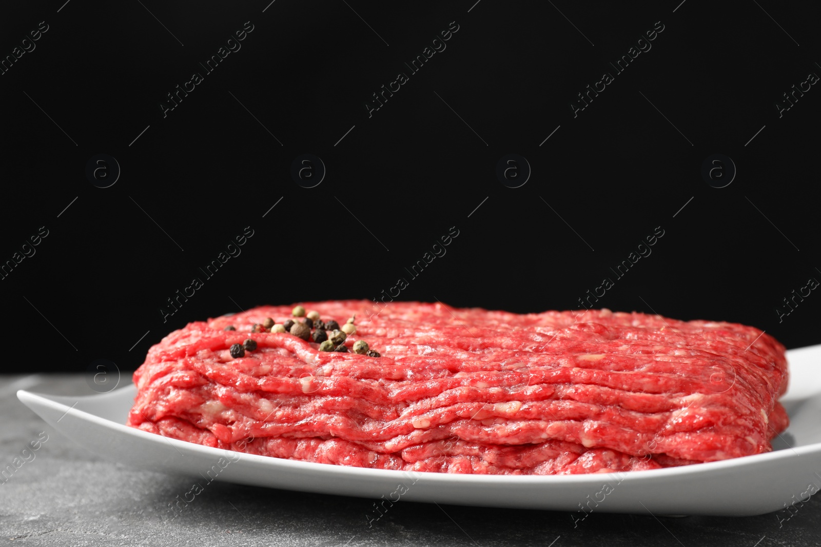 Photo of Raw ground meat and peppercorns on grey table, closeup