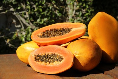 Photo of Fresh ripe cut and whole papaya fruits on wooden table outdoors