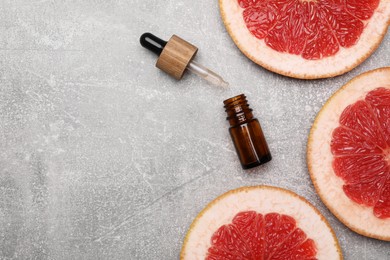 Photo of Bottle of essential oil with grapefruit slices on grey table, flat lay. Space for text