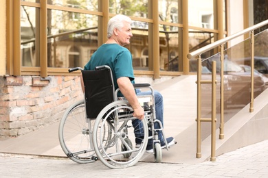 Photo of Senior man in wheelchair using ramp at building outdoors